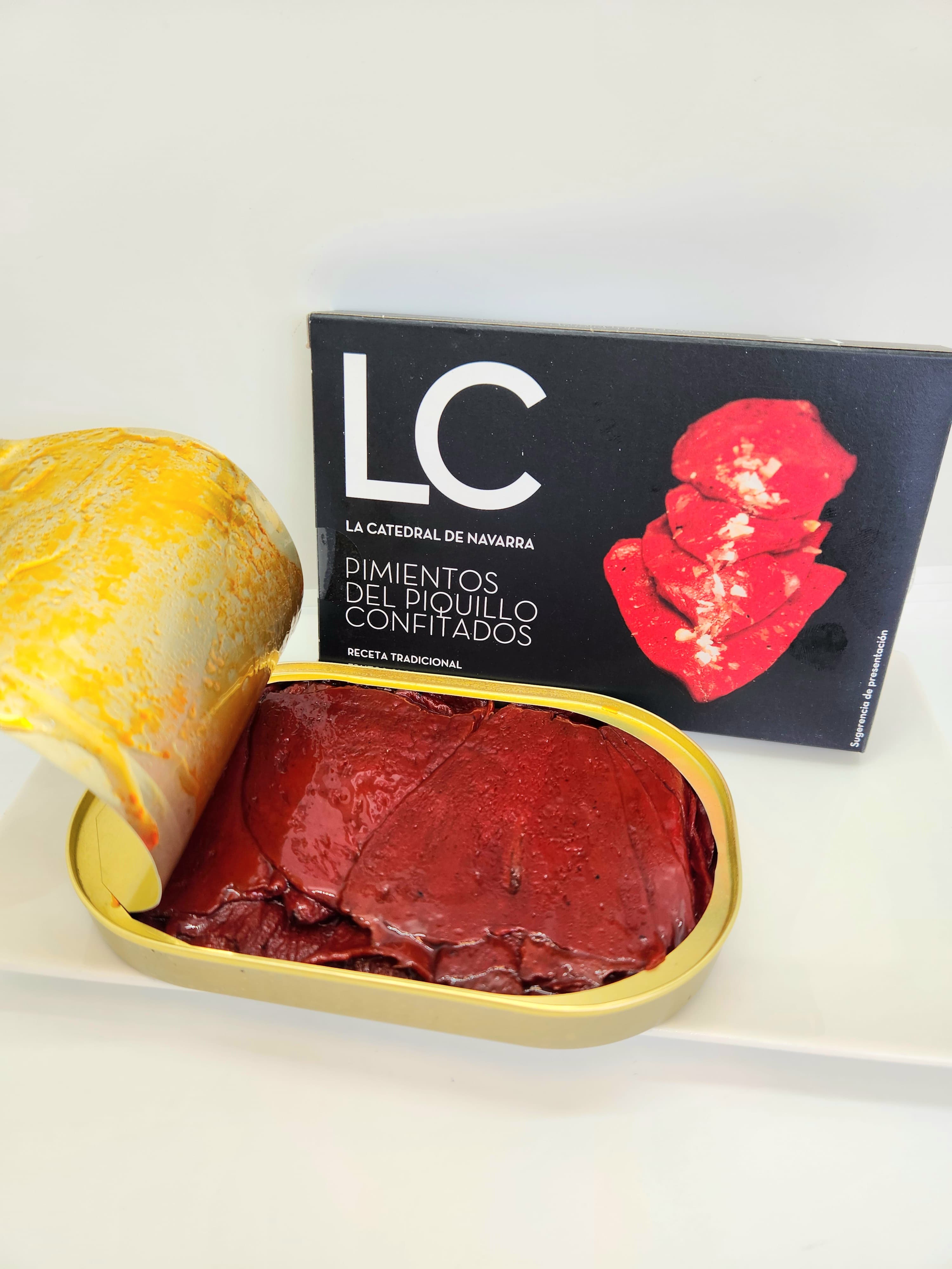 Open gold tin of red piquillo peppers beside its black La Catedral de Navarra packaging.